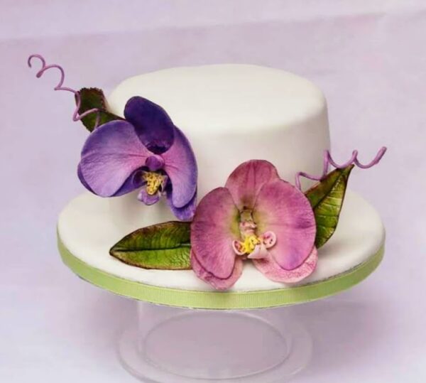 A cake with two beautiful moth orchids on it one pink one purple